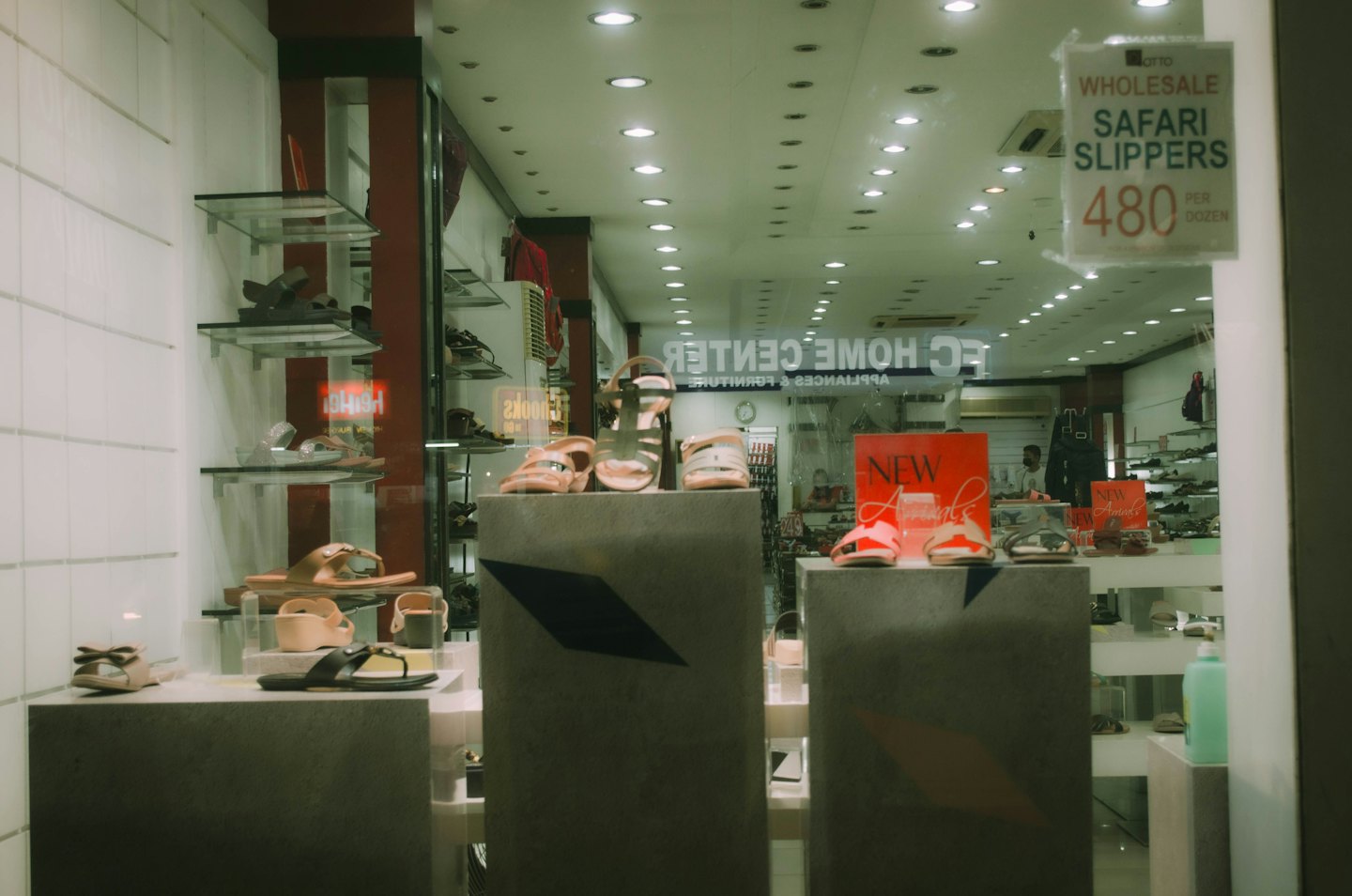 Sandals and slippers displayed on pedestals inside a store window.