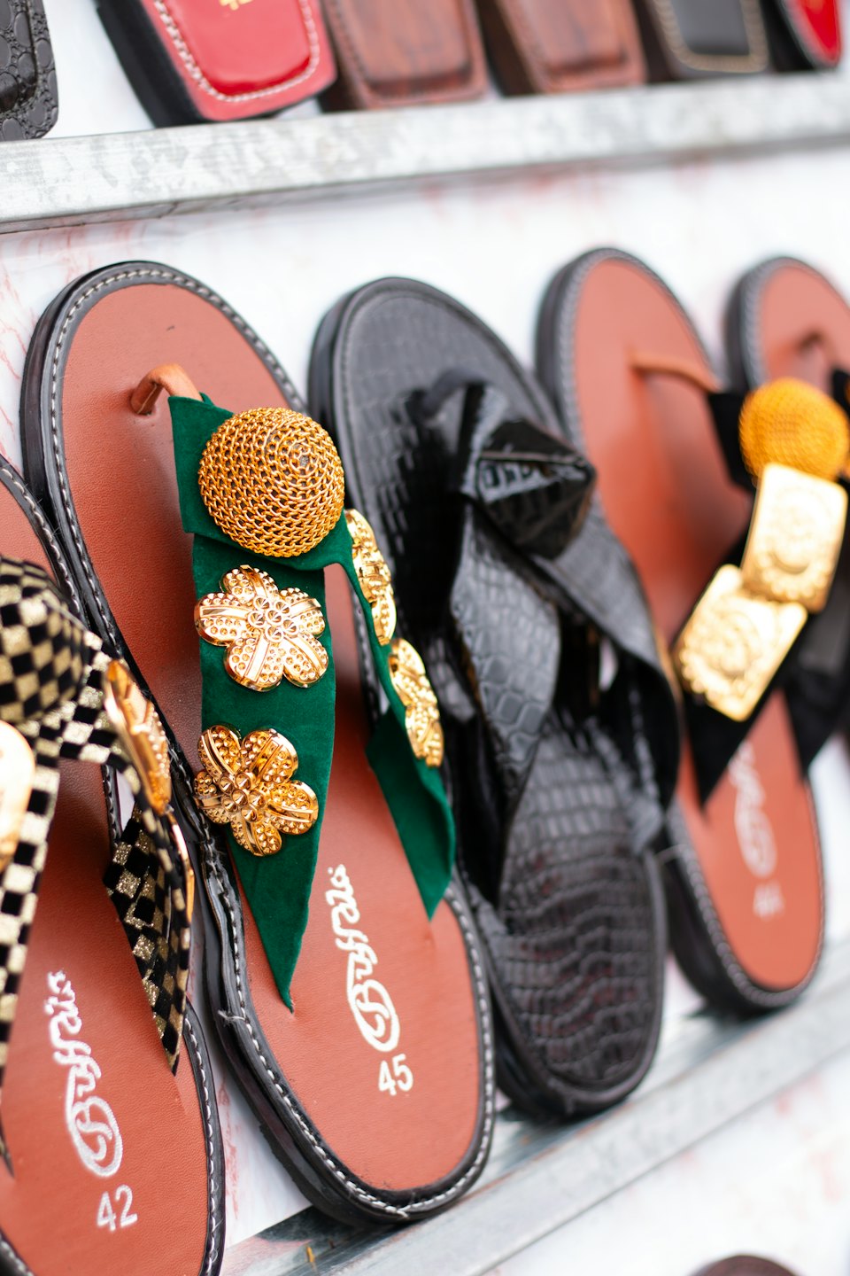 Decorative sandals with gold accents arranged on a metal shelf.
